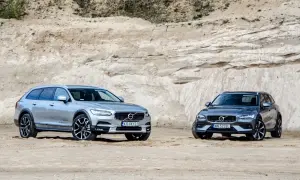 Dwa samochody Volvo Cross Country, srebrny i grafitowy, stoją na piaszczystym podłożu przed piaskową ścianą.