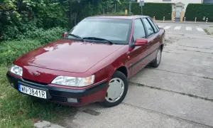 Czerwony Daewoo Espero z tablicą rejestracyjną WN-3841R zaparkowany przy zarośniętym poboczu i betonowej drodze.