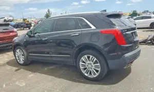 Czarny Cadillac XT5 stoi na placu wśród innych pojazdów.