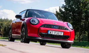 Czerwony Mini Cooper na tle zieleni. Wiele osób szuka opinii o tym modelu, a ten egzemplarz wygląda na gotowy do jazdy.