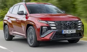 Czerwony Hyundai Tucson N Line, nowoczesna hybryda, pędzi po drodze, otoczony zielenią.