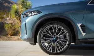 Nowe BMW X5 2023 w kolorze niebiesko-zielonym, z felgami o skomplikowanym wzorze, zaparkowane na tle pustynnego krajobrazu.