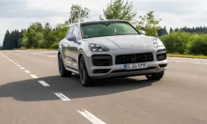 Srebrny Porsche Cayenne 2025 sunie po asfaltowej drodze, otoczony zielenią lasów.
