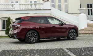 Bordowy BMW iX z eleganckimi felgami stoi przed luksusową posiadłością z kamienną nawierzchnią.