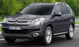 Szary Citroen C-Crosser jedzie po drodze, otoczony zielenią.