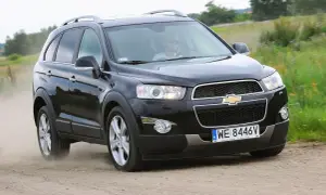 Czarny Chevrolet Captiva jedzie po piaszczystej drodze, wzbijając tumany kurzu. Kierowca w okularach przeciwsłonecznych prowadzi auto przez zielone pola.