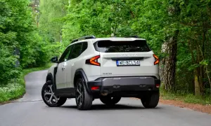 Nowy Dacia Duster 3 na krętej leśnej drodze. Nowoczesne światła i masywna sylwetka podkreślają jego terenowy charakter.