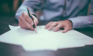Dłoń pisze długopisem na dokumencie. Może to być wypowiedzenie OC w wefox.