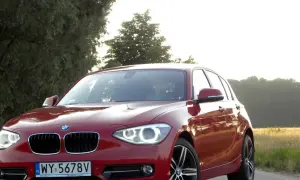 Czerwone BMW 118d na tle drzew i pól.