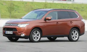 Brązowy Mitsubishi Outlander 3 na tle zielonego wzgórza.