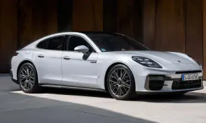 Elegancki, biały Porsche Panamera 2024 z czarnym dachem i przyciemnianymi szybami, zaparkowany na tle rustykalnej ściany.