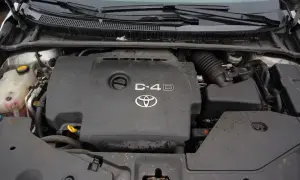 Silnik Toyota Avensis 2.0 D4D, widok z góry. Pokrywa silnika z logo Toyoty i oznaczeniem D-4D.