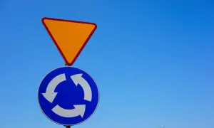 Znak A7 (ustąp pierwszeństwa) i znak C12 (ruch okrężny) na tle błękitnego nieba.