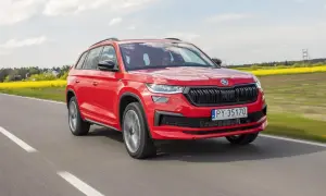 Czerwony Skoda Kodiaq 2023 pędzi po drodze, mijając kwitnące pola rzepaku.
