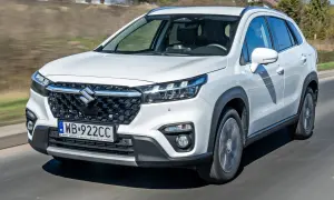 Biały Suzuki S-Cross jedzie po drodze, widoczny przód auta z grillem i światłami.