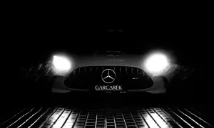 Czarny Mercedes-AMG GT Black Series z włączonymi światłami, stojący na mokrej, metalowej kratce.