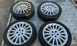 Cztery aluminiowe felgi z oponami zimowymi, z logo Opla, leżące na metalowej platformie.