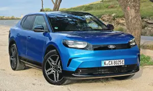 Niebieski Ford Capri 2025, nowoczesny elektryczny SUV, zaparkowany na żwirowej drodze obok drzewa.