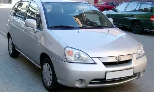 Srebrne Suzuki Liana stoi na ulicy, obok zielonego kombi.