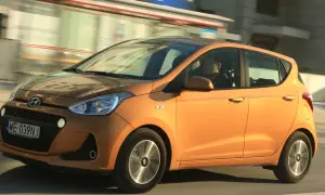 Pomarańczowy Hyundai i10 z kierowcą w środku jedzie ulicą.