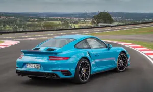 Błękitne Porsche 911 Turbo S na torze wyścigowym, z widokiem na miasto w tle.