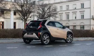 Dwukolorowy Toyota Aygo X na ulicy, z tyłu widoczny budynek z kolumnami.