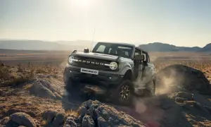 Ford Bronco pokonuje skalisty teren pustyni, wzbijając tumany kurzu.