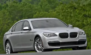 Srebrne BMW 7 F01 na tle zielonych drzew. Elegancka limuzyna prezentuje się okazale na drodze.