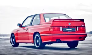 Czerwone BMW E30 Coupe M3 w ruchu, z widocznym spojlerem i podwójnym wydechem.