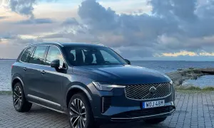Elegancki, ciemnogranatowy Volvo XC90 2025 zaparkowany nad morzem, z chmurami na niebie.