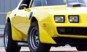 Żółty Pontiac Trans Am z lat 70. z charakterystycznym wlotem powietrza na masce i szerokimi oponami Cooper Cobra.