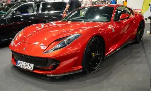 Błyszczący, czerwony Ferrari 812 Superfast z czarnymi felgami na wystawie motoryzacyjnej.