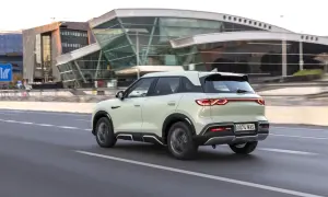 Jasny, nowoczesny BYD atto 2 jedzie po drodze, mijając futurystyczny budynek.