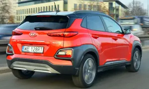 Czerwony Hyundai Kona 2025 z czarnym dachem pędzi po drodze, ukazując swoje nowoczesne tylne światła i masywne nadkola.