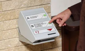 Dłoń naciska przycisk na automacie do wydawania dowodów rejestracyjnych, ułatwiając wymianę dowodu rejestracyjnego online.