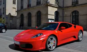 Czerwone Ferrari F430 na brukowanej ulicy przed kamienicą. Zastanawiasz się, ile kosztuje Ferrari? To marzenie wielu kierowców.