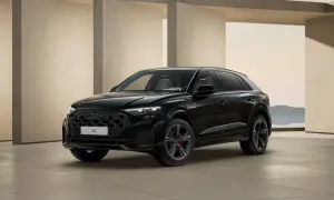 Elegancki, czarny Audi Q8 2025 z czarnym grillem i czerwonymi zaciskami hamulcowymi, zaparkowany przed nowoczesną architekturą.