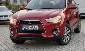 Czerwony Mitsubishi ASX 1.6 benzyna z tablicą rejestracyjną OPR 4AA7 zaparkowany na kostce brukowej.