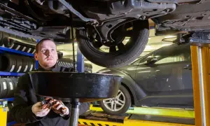 Mechanik wymienia olej w samochodzie, zbierając zużyty płyn do miski.