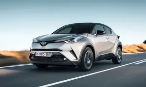 Srebrna Toyota C-HR 2023 pędzi po pustej drodze, z zachodzącym słońcem w tle.