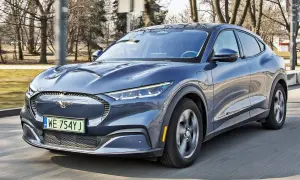 Niebieski Ford Mustang Mach-E jedzie po drodze, z widocznym logo konia na grillu.