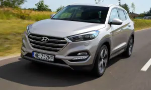 Srebrny Hyundai Tucson 2016 jedzie po drodze, otoczony zielenią.