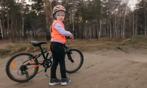 Dziewczynka w kasku i kamizelce pomarańczowej stoi obok roweru, gotowa na egzamin na kartę rowerową.