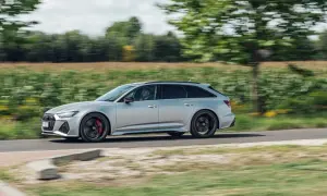 Srebrne Audi RS6 Avant pędzi po wiejskiej drodze, otoczone zielenią pól i drzew.