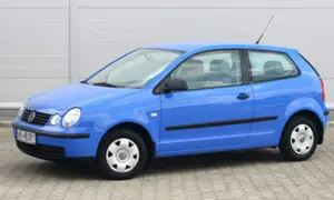 Niebieski Volkswagen Polo 1.2 benzyna, widok z boku. Auto stoi na kostce brukowej przed szarym budynkiem.