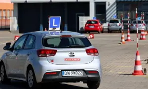 Srebrny samochód z literą "L" na dachu, gotowy do egzaminu. Dofinansowanie do prawa jazdy może pomóc w nauce jazdy na takim pojeździe.
