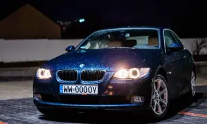 Ciemnoniebieskie bmw 325i z kroplami deszczu na karoserii, zaparkowane nocą na mokrym parkingu.