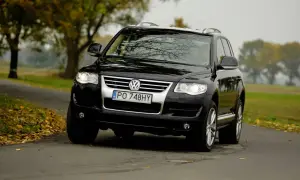 Czarny Volkswagen Touareg 2024 na jesiennej drodze, otoczony drzewami z kolorowymi liśćmi.