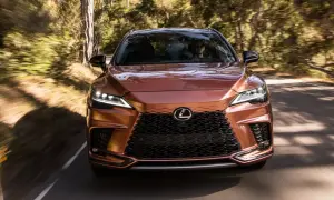 Miedziany Lexus RX 450h pędzi leśną drogą, światła LED rozświetlają trasę.