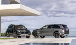 Dwa Mercedesy GLS 2025, jeden zielony, drugi szary, zaparkowane przed nowoczesnym budynkiem z basenem.